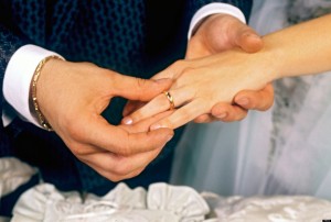 A8KDCT Groom places gold wedding ring on the finger of his new bride in marriage ceremony