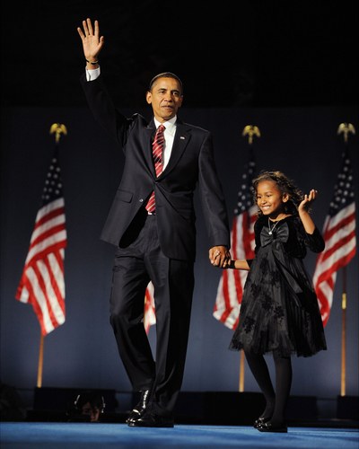 Sasha Obama coordinating with her Daddy for the 2008 election, wearing a black floral-print dress and black suede cardigan with giant bow 